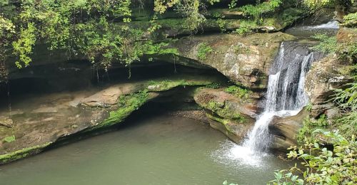 A waterfall is pouring into a pond with a cave in the background.
