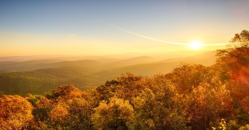 Sunrise in November over scenic mountaintop in Ouachita National Forest, with fall colors, heavy mist and fog in valleys, and sun flares