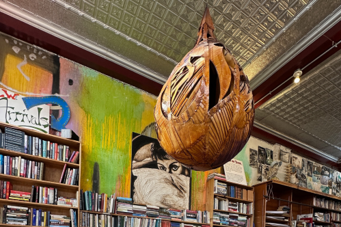 A large wooden sculpture hangs from a tin ceiling in a bookstore.