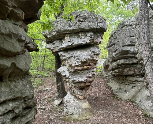 Three large boulders, each with their own jagged, unique shape, in a forested landscape.