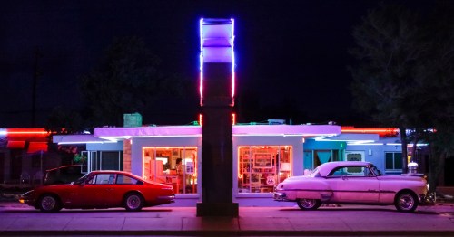 Two older vehicles sit in front of a diner at night in Tucumcari, NM.