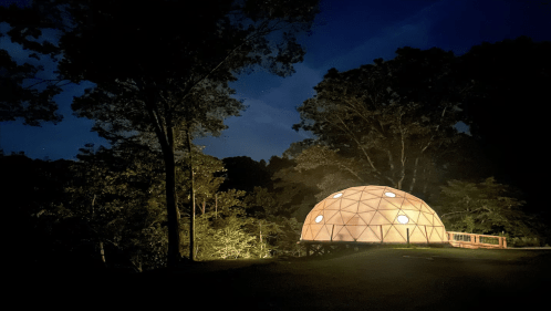 A geo dome Airbnb in West Virginia illuminated at night with trees in the background.
