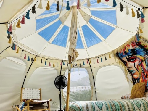 the white interior of a yurt with a bed, fan, and chair
