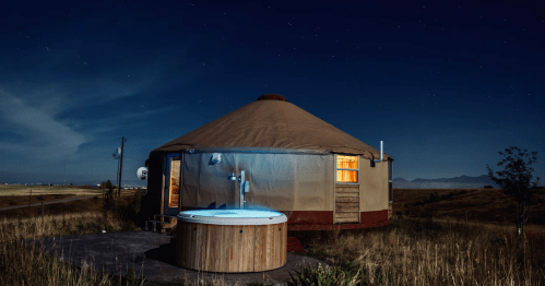 A glowing wood hot tub outside a cozy yurt Airbnb under a starry sky near Bozeman, MT.