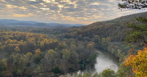 A view from a hiking trail in Pennsylvania overlooking a river and mountains at sunset.