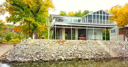 Stilted modern Iowa riverfront Airbnb with sunroom, hot tub, and river access stairs.