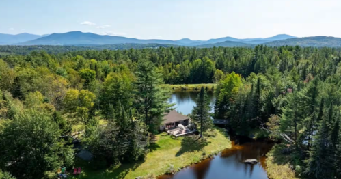 Aerial view of Faraway Pond Airbnb cabin by a lake in the White Mountains, New Hampshire, surrounded by lush forest.