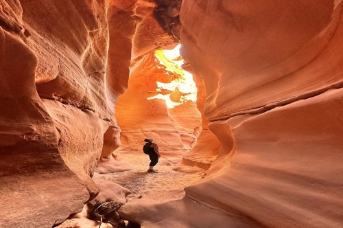 A hiker standing inside a slot canyon in Utah with bright orange walls