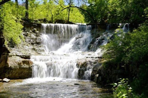 A multi-tier waterfall swimming hole in Kansas with a large pool, surrounded by lush greenery