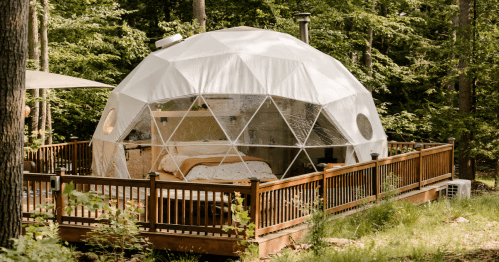 A white geodesic dome glamping rental for stargazing, situated on a wooden deck in a New Hampshire forest.