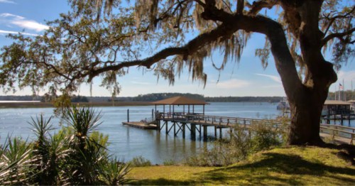 The branches of an oak tree with Spanish Moss frame a pier at an Airbnb in Georgia.