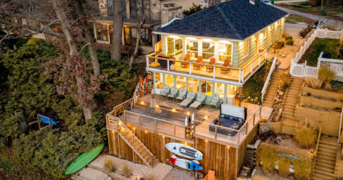 Aerial view of a green Indiana Dunes Airbnb with a tiered wooden deck, hot tub, and kayaks along the lakefront.