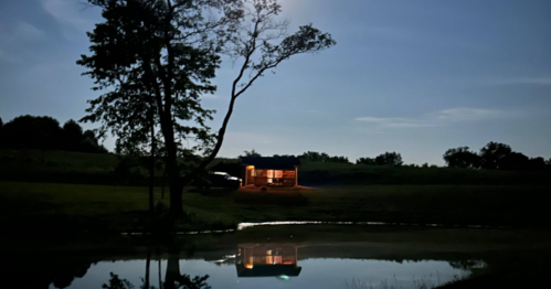 Night view of a warm, lit Iowa cabin by a pond with a clear reflection.