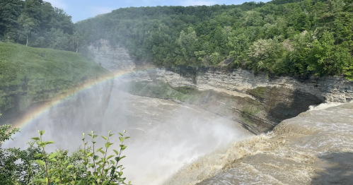 View from Letchworth State Park Lower Falls hiking trail, showing a powerful waterfall with a bright rainbow.