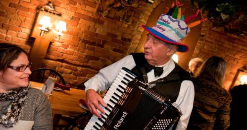A man in a "happy birthday" hat plays an accordion next to a woman at the Munich Haus restaurant in Chicopee, Massachusetts.