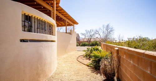 the exterior of a beige-colored Airbnb in New Mexico with a sandy walkway and green plants on the side