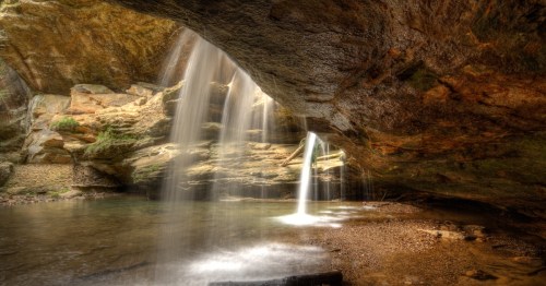 Waterfall cascading under a rock overhang at Old Man's Cave hiking trail in Hocking Hills, Ohio.