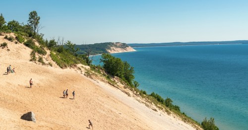 Hikers climbing massive sand dunes over Lake Michigan at Sleeping Bear Dunes National Lakeshore.