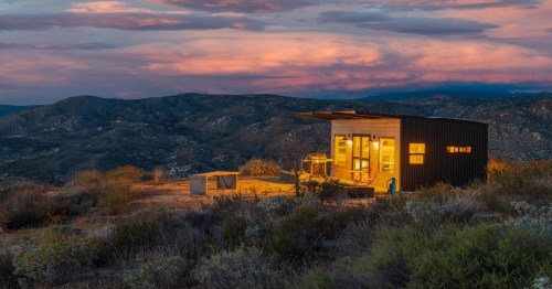 a luxurious tiny home on the hills in southern california with bright yellow-tinted lights on inside the house during dusk