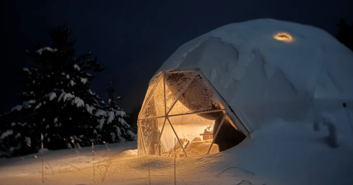 Snowy geodesic dome glamping in Michigan, warmly lit at night.
