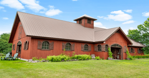 Red Road Farm Bunkhouse, a renovated red barn Airbnb with a cupola and shutters on a green lawn in Stowe, Vermont.