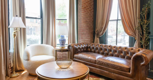 Cozy Providence Airbnb flat with a leather Chesterfield sofa, bouclé chair, and exposed brick wall.