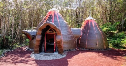 two-volcano shaped figures of a hawaiian airbnb with trees in the background and a red-colored ground