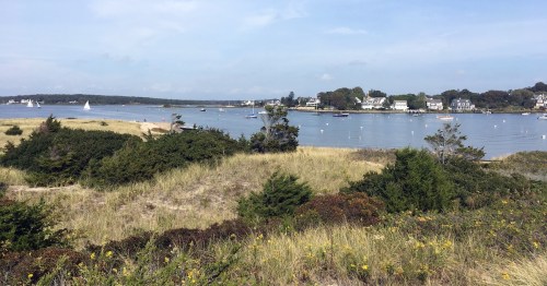 Coastal view of Watch Hill, Rhode Island, with large waterfront homes, sailboats in the water, and dunes.