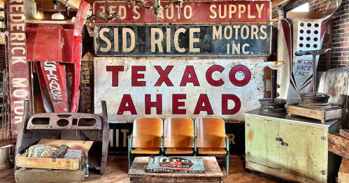 a large "auto supply/texaco ahead" sign hangs on the wall in back of a set of 3 wood stadium shairs, a wood table, and other salvage items from West End Architectural Salvage & Coffee Shop in Des Moines, Iowa