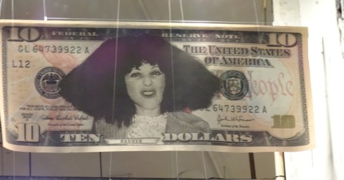 A $10 bill featuring comedian Gilda Radner as Roseanne Roseannadanna with big hair and a funny expression.