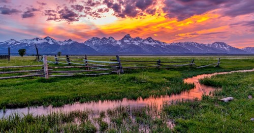 a golden and pink sunset above the mountains, grassy fields, and small creek in wyoming