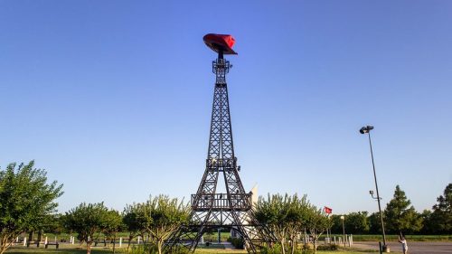 The eiffel tower in Paris, Texas with a red cowboy hat on top of it against a blue sky