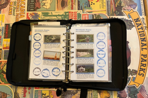 A National Parks passport binder with several cancellation stamps is laid out on a National Parks poster.