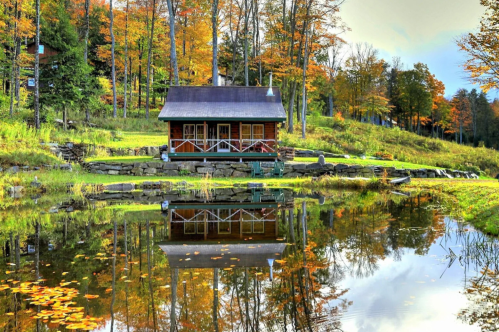 An autumn view of the exterior of the Trout Pond VRBO rental in Londonderry, Vermont. The cabin is reflected in the property's pond.