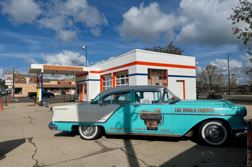 a teal and white historic car sits in the parking lot outside pete's gas station museum in williams az