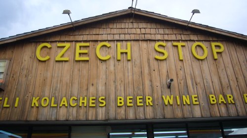 Exterior of Little Czech Bakery and Czech Stop, featuring a busy parking lot and colorful signage.