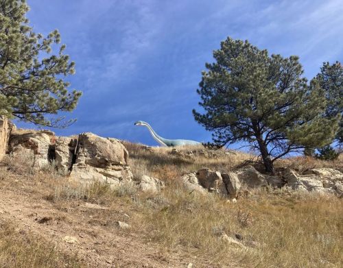 A life-size concrete dinosaur on a hill with trees.