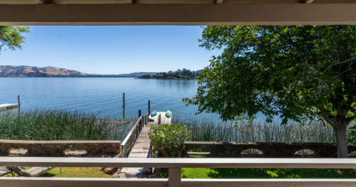 From a back porch, a private walkway leads to a wooden dock that extends into a tranquil, blue lake.