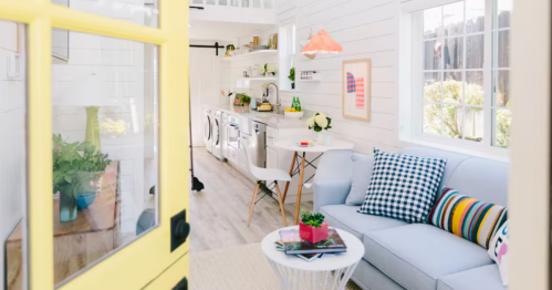 A yellow door opens into a brightly furnished tiny home.