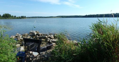A camping chair and fishing pole overlooking a lake.