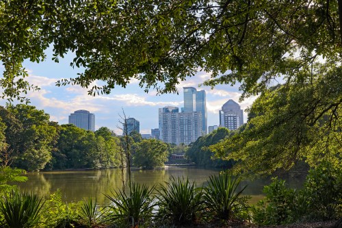 The Atlanta skyline peeks over a large scenic pond, surrounded by trees and greenery.