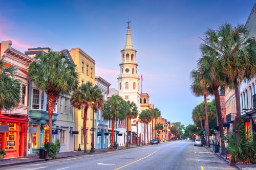 A cityscape of Charleston, South Carolina, where colorful buildings and palm trees line the streets.
