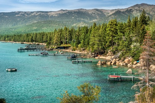 Scenic nature view of boats docked over the calm waters of Lake Tahoe from the rocky boulders on shore in summer