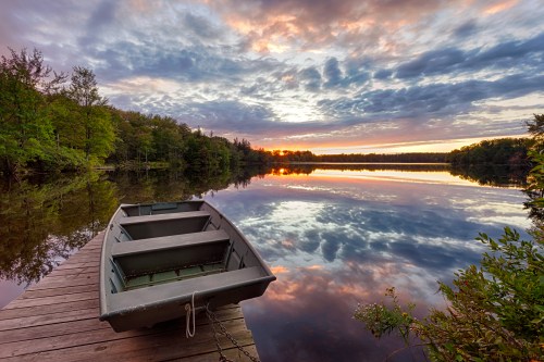 Rowboat tied to a wooden dock at sunset on a lake, with trees and clouds reflected in the water at Promised Land State Park.