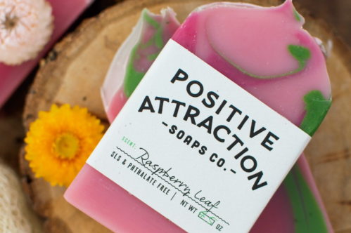 Raspberry Leaf soap bar from Positive Attraction Soaps Co. sitting on a wooden slab with a yellow flower