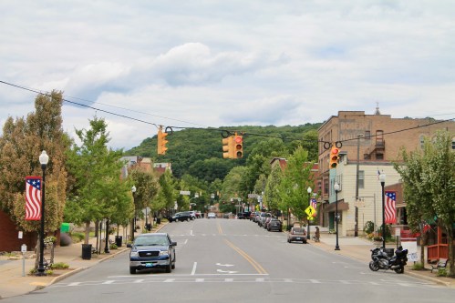 Ridgway, PA downtown street with trees, cars, and traffic lights.