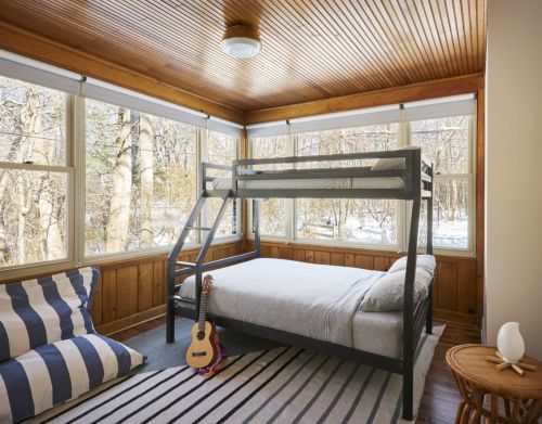 A room with bunk beds and wood paneling overlooking a forest.