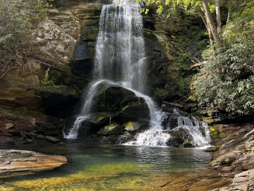 Water rushes over a large waterfall into a idyllic swimming hole at Catawba Falls.