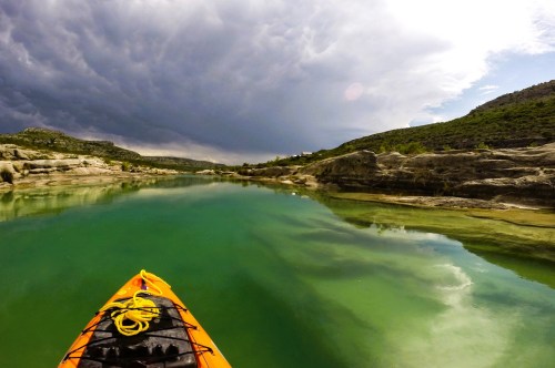Scene of a kayak floating on a river in a remote destination in Texas, with views of high cliffs in the distance.