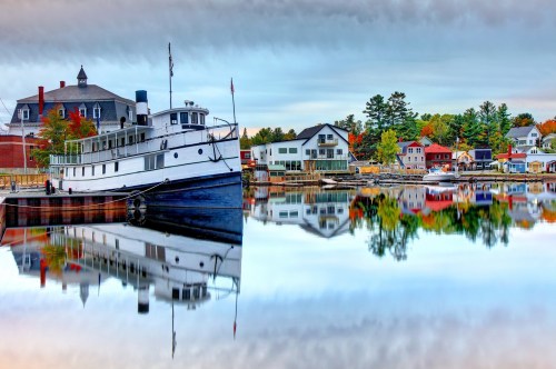 Views of a scenic lake in Maine with a steamboat and houses reflecting off the surface.
